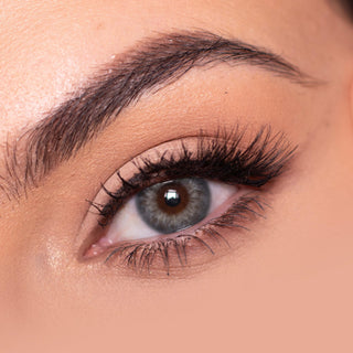 Close-up shot of a model eye wearing Sugarlook Grey colored contact lens in one eye that is naturally dark-brown with natural eye make up