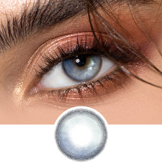 Close-up shot of a model eye wearing sunlit deep blue colored contact lens in one eye that is naturally dark-brown with natural light gold eye make up