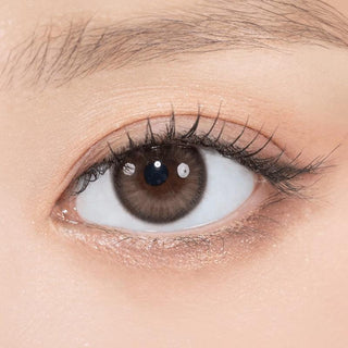 Close-up shot of model's eye adorned with Gemhour Theia Glow Brown color contact lenses with prescription, complemented by minimalist eye makeup, showing the brightening and enlarging effect of the circle contact lens on dark brown eyes.