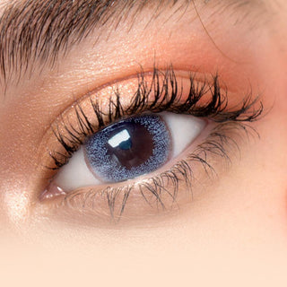Close-up image featuring a model wearing Toronto Grey contact lenses over dark brown irises, accompanied by naturally curled lashes and peach eyeshadow.