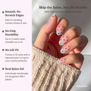 A hand shows EyeCandys Unbothered Press-On Nails—short, almond-shaped with a nude base, red polka dots, and a blue accent tip. Enjoy salon gel quality, no-chip durability, a no-lift fit, and reusable wear.