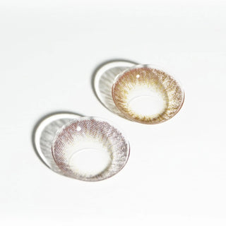 Two colored contact lenses from EyeCandys Pink Label Vintage Grey are placed on a white surface, casting soft circular shadows.