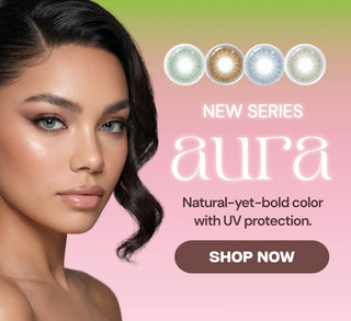 Promotional banner for the Aura contact lens series featuring a model wearing light gray lenses, four lens color options, soft pink and green gradient background, and a Shop Now button.