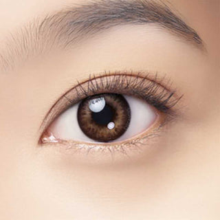 A close-up of a brown eye with long lashes and smooth, light skin shows the wearer using Bausch & Lomb Lacelle Baby Brown (30pk) coloured contact lenses. The eyebrow appears at the top of the image.