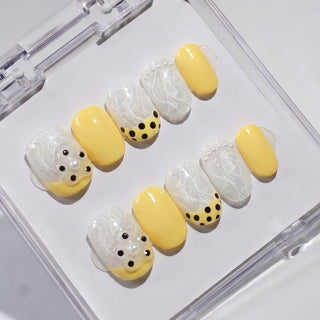 EyeCandys Bananito press on nails featuring bright yellow nails with embedded white lace gel, black polka dot tips, pearl beads, and crystal accents.