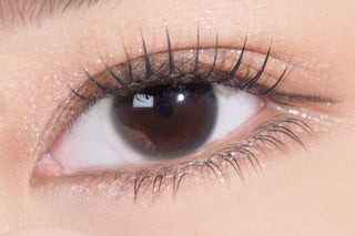 A close-up of a human eye with long eyelashes and smooth skin, showing detailed texture of the iris, eyelid, and surrounding area. The eye is wide open and reflects light.