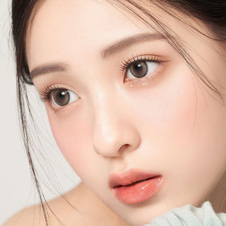Asian model demonstrating a K-idol-inspired look with 1-Day Pebble Grey coloured contact lenses, highlighting the instant brightening and enlarging effect of the circle contact lenses over dark irises.