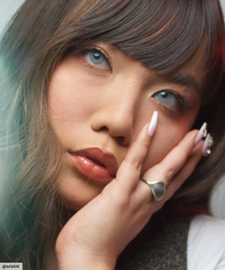 A female model with natural dark eyes wearing eyecandys dare to be blue contact lenses, complemented by pink eyeshadow and peach lipstick