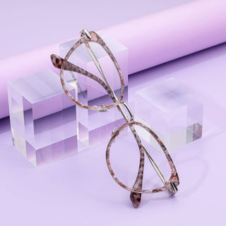 The EyeCandys Aura Cat Eye frames, in a chic pinkish-brown tortoiseshell, are displayed on clear acrylic blocks against a pastel purple background.