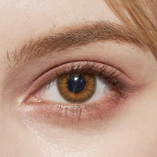 Close-up of model’s eye wearing EyeCandys Pink Label Flirty Orange Brown contact lens, complemented by peach eyeshadow – natural, soft glam look