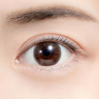 Close-up shot of model's eye adorned with Feliamo 1-Day Cafe Mocha (10pk) color contact lenses with prescription, complemented by minimalist eye makeup, showing the brightening and enlarging effect of the circle contact lens on dark brown eyes.