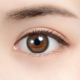 Close-up shot of model's eye adorned with Feliamo 1-Day Coffee Jelly (10pk) color contact lenses with prescription, complemented by minimalist eye makeup, showing the brightening and enlarging effect of the circle contact lens on dark brown eyes.