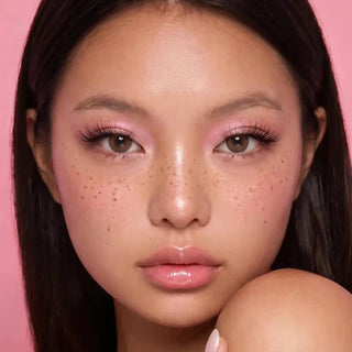 Woman with long brown hair and freckles wearing EyeCandys Pink Label Marshmallow Brown colored contact lenses with soft pink makeup, showcasing a warm natural brown eye color for an effortless everyday look.