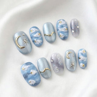 Gilded Cirrus press on nails by EyeCandys featuring sky blue cat eye base with hand painted cloud details and metallic gold celestial moon and star charms.