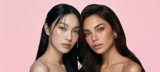 Two women posing against a pink background wearing light blue and green colored contacts.