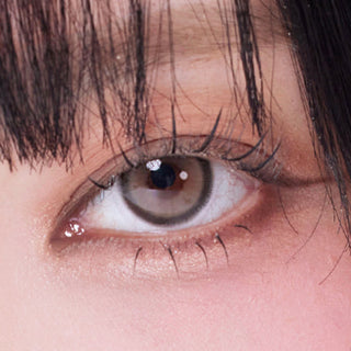 Close-up shot of model's eye adorned with Eyesm Hugmoon 1-Day Grey (10pk) prescription colored contacts, complemented by clean eye makeup, showing the brightening effect of the prescription cosmetic contact lens on dark brown eyes.