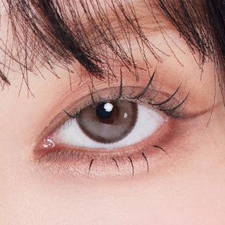 Close-up shot of model's eye adorned with Eyesm Hugmoon Dusty Brown prescription colored contacts, complemented by clean eye makeup, showing the brightening effect of the prescription cosmetic contact lens on dark brown eyes.