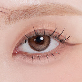 Close-up shot of model's eye adorned with Eyesm Hugmoon 1-Day Brown (10pk) prescription colored contacts, complemented by clean eye makeup, showing the brightening effect of the prescription cosmetic contact lens on dark brown eyes.