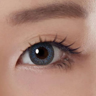 Close-up shot of a model eye wearing Lacelle Colors Majestic Blue colored contact lens in one eye that is naturally dark-brown with natural eye make up and long lashes