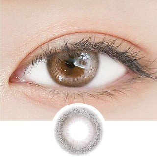 Close-up shot of a model's eye wearing Lensrang Credit Ash Brown color contacts with prescription, paired with K-beauty-inspired eye makeup, showing the brightening and enlarging effect of the circle contact lens on dark brown eyes, above a cutout of the contact lens pattern with limbal ring on a white background.