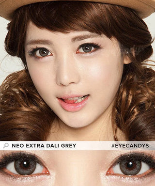 A young woman with curly brown hair wears a brown hat and NEO Vision Extra Dali Grey color contact lenses by NEO Vision, smiling playfully. A close-up highlights the grey lenses in her eyes with text: "NEO EXTRA DALI GREY #EYECANDYS.