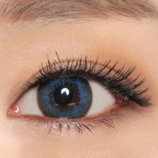 A close-up of a human eye with long lashes, nude eyeshadow, and vibrant NEO Vision Extra Dali Blue circle lenses by NEO Vision covering the iris.