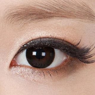 A close-up of an eye with long lashes, subtle shimmery eyeshadow, black upper eyeliner, and NEO Vision Extra Dali Black circle lenses by NEO Vision for a striking effect. The eyebrow is visible above the eye.