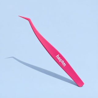 Pink EyeCandys Hasom lash tweezer displayed on a blue surface, showcasing the non-stick eyelash applicator tool.
