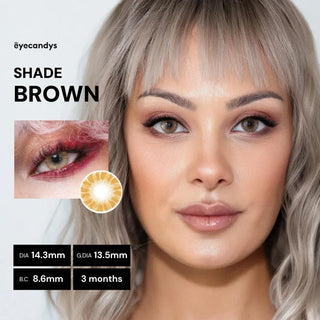 A woman with light gray-blonde hair wears EyeCandys Shade Brown contacts. The image shows her face, a close-up of her eye, the lens, and product details about diameter, base curve, and duration from the EyeCandys brand.