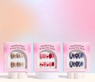 EyeCandys press on nails assortment on pink backdrop showcasing trending reusable nail sets with floral, chrome, marble, and glitter nail designs.