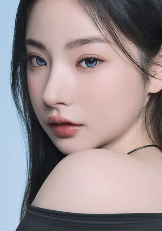 A female model with natural dark eyes wearing i-Sha Reborn Reborn Sky Veil contact lenses, complemented by subtle eyeshadow and peach lipstick