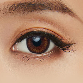 Model's eye wearing the Acuvue Define Natural Shine Brown prescription color contact lens with light eye makeup, showing the widening effect of the circle lens on a dark iris.