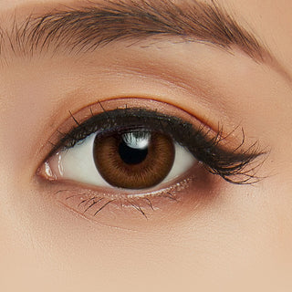 Model's eye wearing the Acuvue Define Radiant Chic Brown prescription color contact lens with light eye makeup, showing the widening effect of the circle lens on a dark iris.