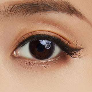 Close-up shot of a model eye wearing Lacelle Modest Black colored contact lens in one eye that is naturally dark-brown with natural eye make up and long lashes