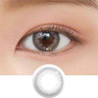 Close-up shot of model's eye adorned with Chuu Cloud Pudding Grey (10pk) daily color contact lenses with prescription, complemented by clean eye makeup, showing the brightening and enlarging effect of the circle contact lens on dark brown eyes, above a cutout of the contact lens pattern with limbal ring on a white background.