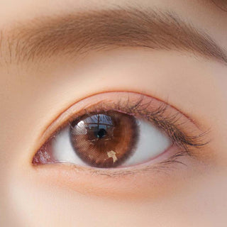 Close-up shot of model's eye adorned with Chuu Cloud Pudding Pink Brown (10pk) color contact lenses with prescription, complemented by minimalist eye makeup, showing the brightening and enlarging effect of the circle contact lens on dark brown eyes.