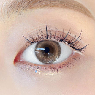 Close-up shot of model's eye adorned with Chuu Milk & Tea Cream Brown color contact lenses with prescription, complemented by minimalist eye makeup, showing the brightening and enlarging effect of the circle contact lens on dark brown eyes.