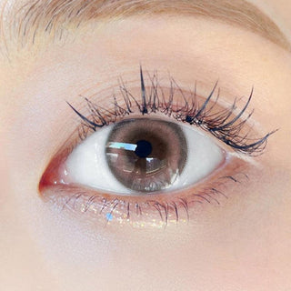 Close-up shot of model's eye adorned with Chuu Milk & Tea Cream Pink color contact lenses with prescription, complemented by minimalist eye makeup, showing the brightening and enlarging effect of the circle contact lens on dark brown eyes.