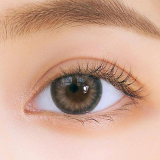 Close-up shot of model's eye adorned with Chuu Sunny Cookie Grey color contact lenses with prescription, complemented by minimalist eye makeup, showing the brightening and enlarging effect of the circle contact lens on dark brown eyes.