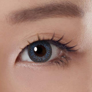 Close-up shot of a model eye wearing Lacelle Colors Majestic Blue colored contact lens in one eye that is naturally dark-brown with natural eye make up and long lashes