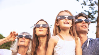 A family of four outdoors wearing paper solar eclipse glasses and looking up at the sky.