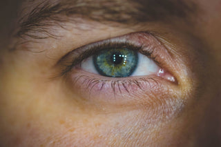 Close-up of an eye featuring a blue and green iris with light reflections around the pupil.