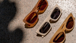 Three pairs of sunglasses with beige, brown, and cream frames resting on a sunny stone surface.