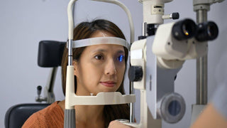 A woman rests her chin on an eye examination slit lamp with blue light illuminating her eye.