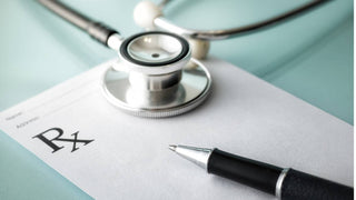 A stethoscope and a black pen lie on a white Rx prescription pad on a light teal surface.