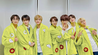 Seven NCT members pose together in matching lime green robes as a backstage k-pop outfit.