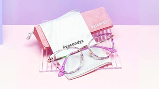 Eyecandys purple patterned cat eye glasses resting on a white pouch and pink case.
