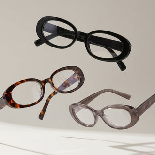 Three pairs of oval eyeglasses in different colors—black, tortoiseshell, and translucent gray—are floating against a neutral background with soft shadows.