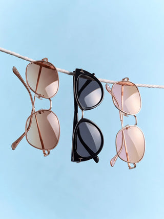 Three pairs of oval eyeglasses in different colors—black, tortoiseshell, and translucent gray—are floating against a neutral background with soft shadows.
