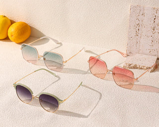 Three pairs of trendy EyeCandys Bermuda Oversized Square Sunglasses with gradient lenses are displayed on a textured surface with two lemons in the background. The first pair has blue-to-clear lenses, the second pair showcases Pink Swizzle colors, and the third pair has black-to-clear lenses.